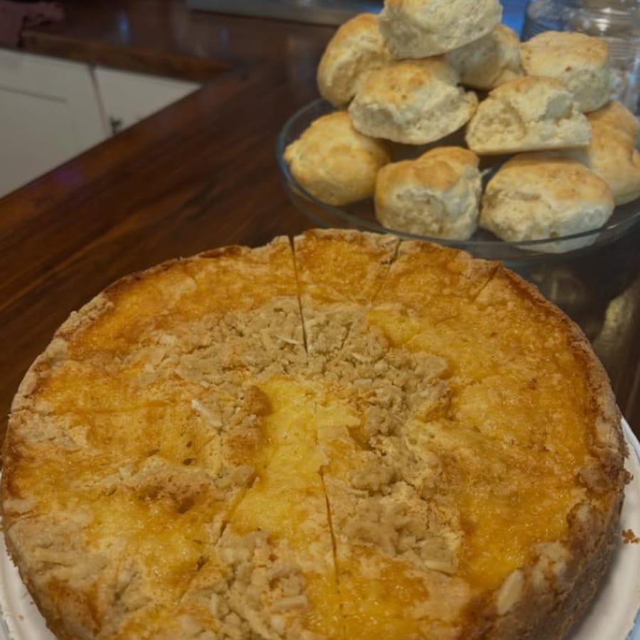A golden baked tart, sliced and ready, with scones on a stand behind